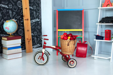 Red tricycle with basket apples. Back to school. Elementary school. Chalkboard, Books, globe in...