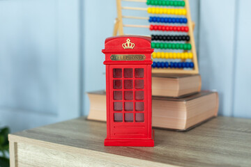 Mini figurine of London Telephone Booth for sale as souvenir. Telephone booth present. Red british phone booth statuette decoration room. 
Figurine of a red telephone booth on shelf. 