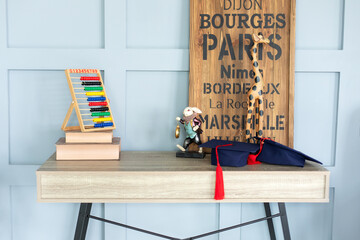 Modern interior study room for child. Desk in a child bedroom. Books, abacus, board, masters hats on wooden table. Concept for Teacher Day, copy space. Back to school, education concept. 