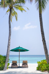 Two sun loungers and a sun umbrella on the background of the beach in the Maldives