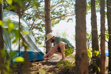Naklejka na ściany i meble caucasian man wearing a hat putting up a tent. Family camping concept