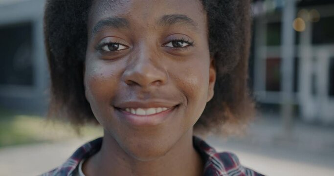 Close-up portrait of cheerful African American person looking at camera with happy smile outdoors in city. Millennials and positive emotion concept.