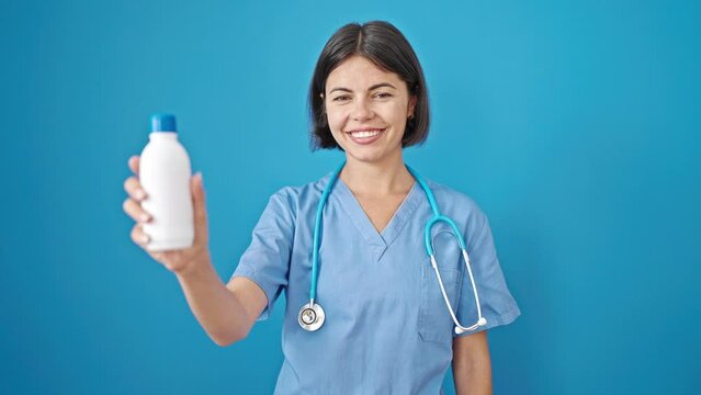 Young beautiful hispanic woman doctor smiling confident holding medicine bottle over isolated blue background