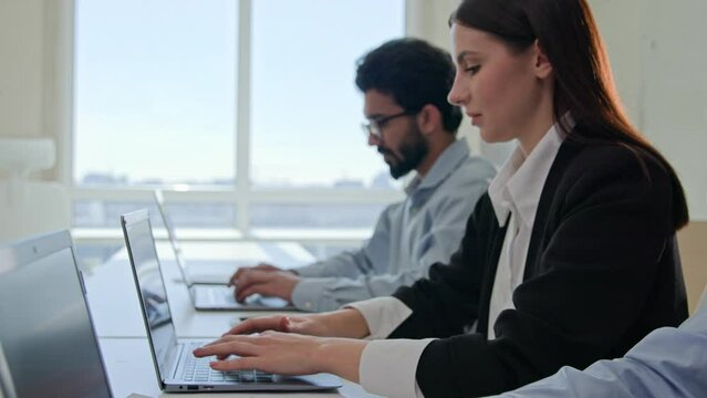 Moving shot row of multiethnic business people typing laptop pressing buttons on computer in modern office focused team managers staff businesswoman and businessmen working remote in coworking company