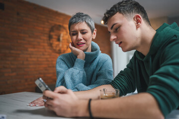 teenage boy and mature caucasian woman sit together at the kitchen at home talk mother and son or...