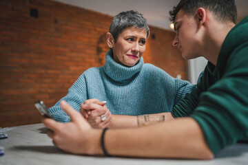 teenage boy and mature caucasian woman sit together at the kitchen at home talk mother and son or...
