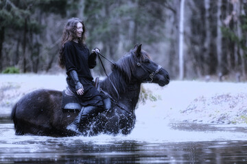 black dressed young woman sitting on a horse that's on its hind legs in the lake
