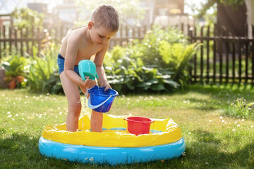 Portrait of little boy play with water in swimming pool. Toddler child have fun in sunny summer garden with inflatable pool. Kid play outdoors. Sweet family time and Happy childhood concept.