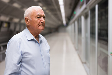 European old man standing in subway station and waiting for train.