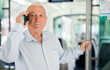 Old European man standing in streetcar and having telephone conversation.