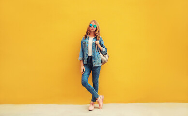 Full length beautiful young woman wearing denim jacket, backpack on yellow background