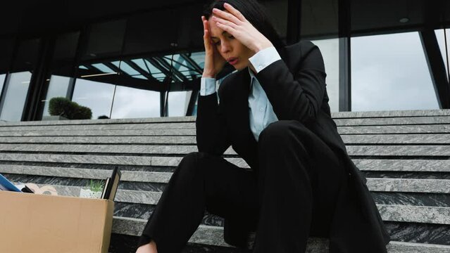 A woman sits on cardboard boxes on the steps outside, feeling the uncertainty and insecurity of her workless situation after job loss. Fired Woman Sitting on Steps with Loss of Work