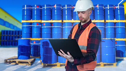 Chemical factory worker. Man factory technologist with laptop. Barrels behind worker. Guy is...