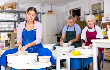 Female artisan in ceramics workshop with pottery wheel and various clay vessels