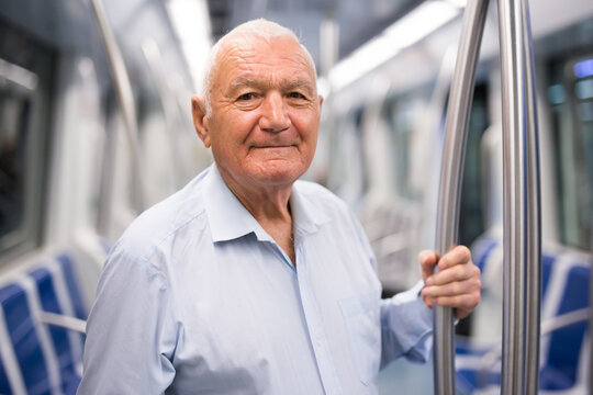 Senior man holding handrail while standing inside subway train.