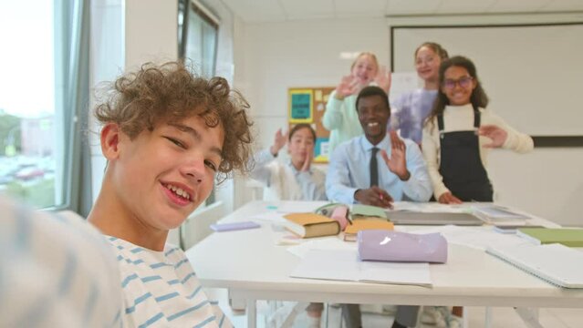 Handheld POV of Biracial curly haired schoolboy recording video blog od himself, his multiethnic classmates and Black male teacher studying together in modern classroom