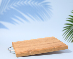 Wooden empty cutting board at an angle on a blue background, kitchen utensils