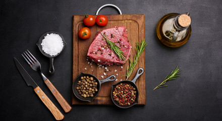 Fototapeta na wymiar Raw piece of beef with spices pepper, rosemary sprig, salt and olive oil on a wooden board, black background