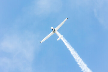 Top view of a gliders plane flying and doing tricks and stunts over the blue sky with white steam wake on a summer day at Gijon air show festival