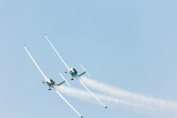 Front view of two white gliders in hazardous formation doing tricks and stunts over the blue sky with white steam wakes on a summer day at Gijon air show festival