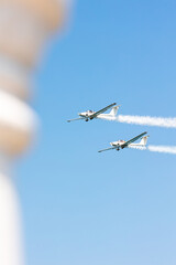 Two white gliders in formation doing tricks and stunts over the blue sky with white steam wakes on a summer day at Gijon air show festival