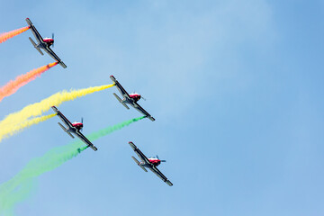 Airplanes squadron in arrow formation doing tricks and stunts over the blue sky with color wakes on a summer day at Gijon air show festival