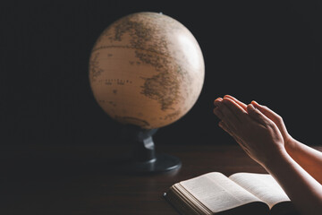 Christian woman praying for globe and people around the world on wooden table with bible. Christian...