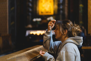 Woman praying on her knees in an ancient Catholic temple to God. Hands folded in prayer concept for...