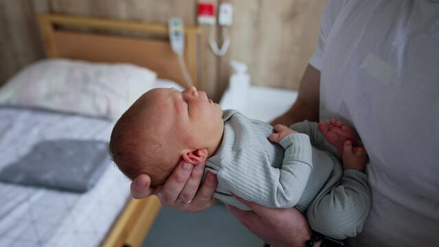 Strong male hand holding a cute tiny child. Father taking care of his newborn baby in maternity hospital.