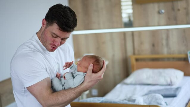 Strong muscular Caucasian man swinging his child on one hand. Happy dad kisses his newborn baby tenderly.
