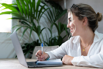 Portrait of smiling millennial caucasian female student sit at desk at home study online on laptop. Happy young cheerful woman use computer take distant course or training. Education concept.