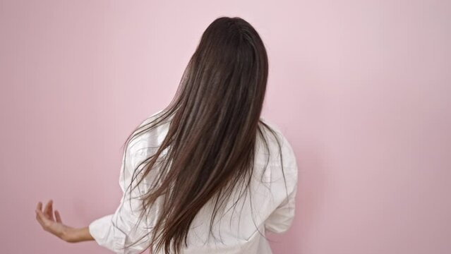 Young beautiful hispanic woman combing hair with hands over isolated pink background