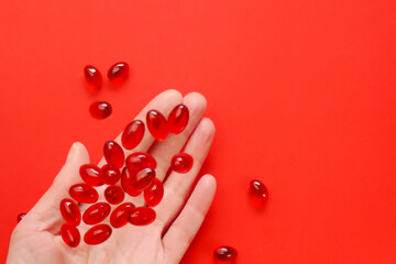 Krill oil capsules in a womans hand on a red background .omega fatty acids.Healthy eating and food supplements. Flying gelatin red krill oil capsules. Dietary supplements and food supplements