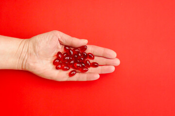 Krill oil capsules in a womans hand on a red background .Healthy eating and food supplements....