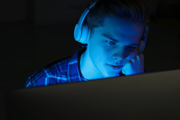 Teenage boy in headphones using computer at night. Internet addiction