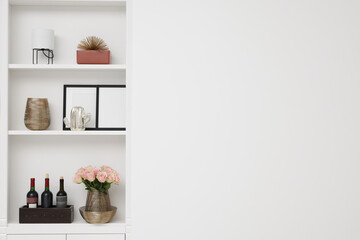 Shelves with different decor near white wall, space for text. Interior design