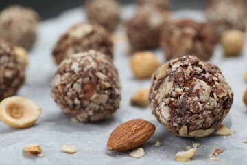 Delicious sweet chocolate candies and nuts on parchment paper, closeup