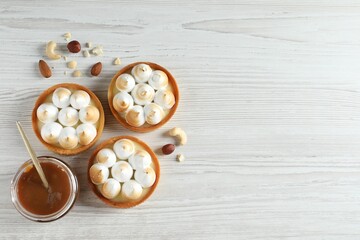 Tasty dessert. Tartlets with meringue, nuts and boiled condensed milk on white wooden table, flat lay. Space for text