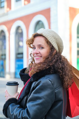 Young caucasian woman looking at camera and smiling holding shopping bags and a coffee cup in winter.