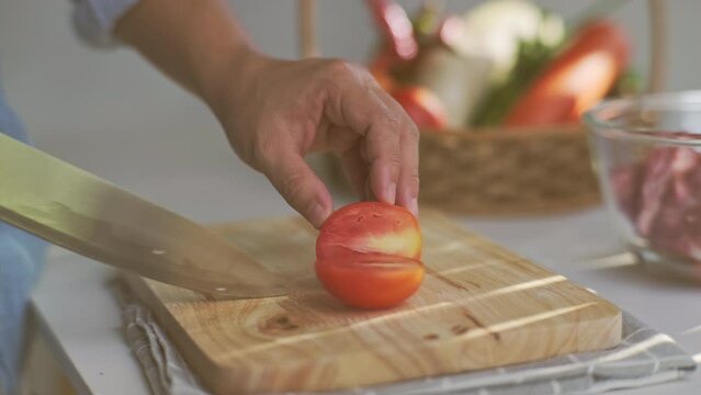 Cooking - Chef's hands are cutting tomatoes on the chopping board in the kitchen. Preparing pork stock with vegetables (broth) in a pot. Homemade bouillon recipe.