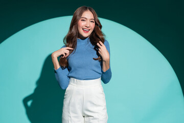 Smiling optimistic Asian casual female woman in blue sweater hand playing fun gesture carefree relax leisure joyful fashion positive thinking portrait shot studio shooting on blue colour background