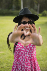 heart gesture with hands young latin woman with long hair wears sunglasses and hat, joy and lifestyle in female model