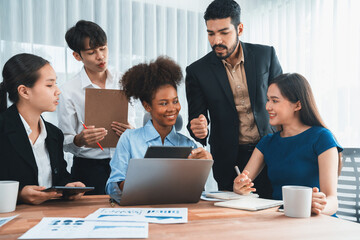 Multiracial analyst team use BI dashboard data to analyze financial report on meeting table. Group of diverse business people utilize data analysis by FIntech for success business marketing. Concord