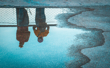 Two people standing above reflection in water puddle on road