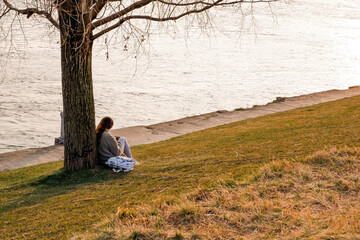 Woman in long sleeve shirt sitting under tree on green grass field near river
