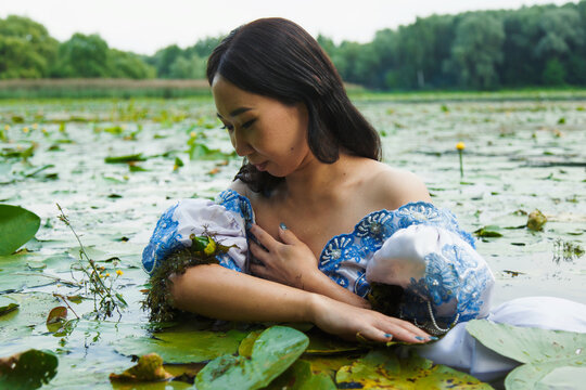 Woman in blue and white floral dress floating in water with green leaves