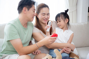 Happy family with daughter play doctor or nurse checkup and examining fever with father on sofa in living room at home, dream child, kid with imagination and playful, lifestyles and medical concept.