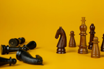 Black and wooden Chess pieces on isolated yellow background, used for success and stategy concept