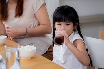 Happiness family with mother and adorable daughter drinking milk or beverage together in the living room at home, bonding and relation, children and mom, nutrition and healthy, lifestyles concept.
