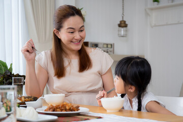 Obraz na płótnie Canvas Happiness asian family mother and daughter eating food in kitchen together at home, parent and kid sitting dining in living room, bonding and relation, lifestyles and nutrition concept.